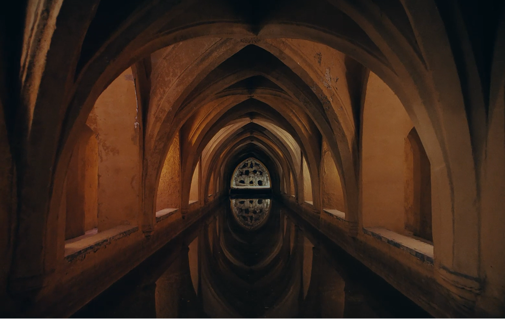 Historic arched corridor reflected in still water, showcasing traditional Andalusian architecture and symmetry.