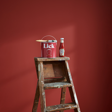 Paint roller and Lick x Heinz paint tin positioned against a deep red wall during painting.