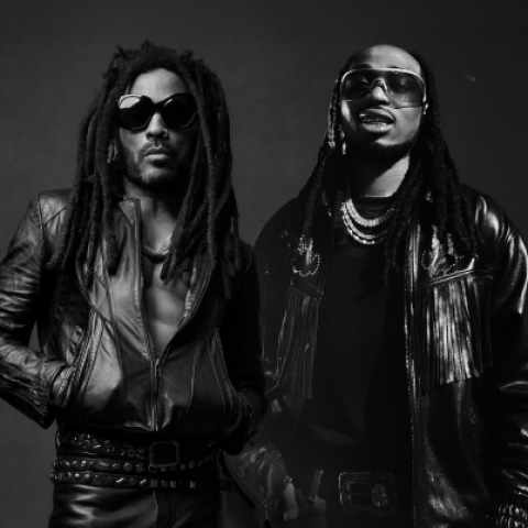 Black-and-white portrait of musicians Lenny Kravitz and Quavo standing side by side in leather jackets and sunglasses against a dark studio background.