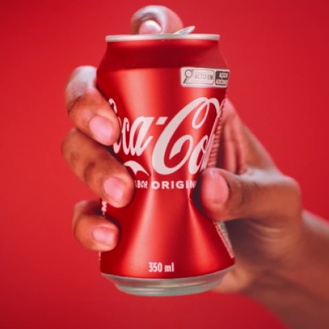 Close-up of a Coca-Cola can held in a hand with a solid red background.