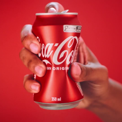 Hand holding a red Coca-Cola can against a red background as part of the Recycle Me campaign.