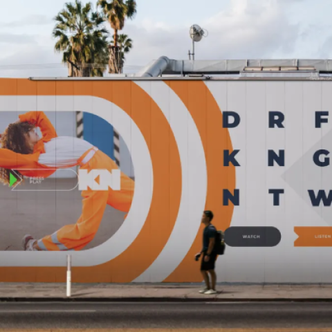 DraftKings Network outdoor mural featuring bold orange and green graphics with athletes in motion and interactive watch, listen, and play prompts.