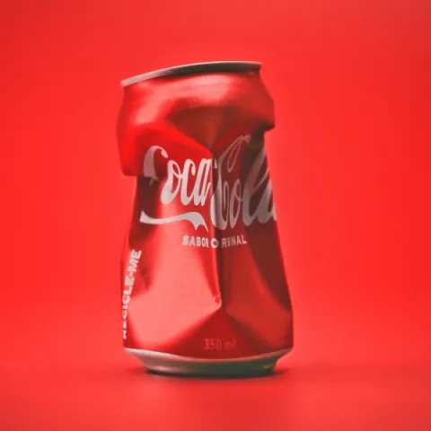 A crushed red coca-cola can pictured on a red back drop.