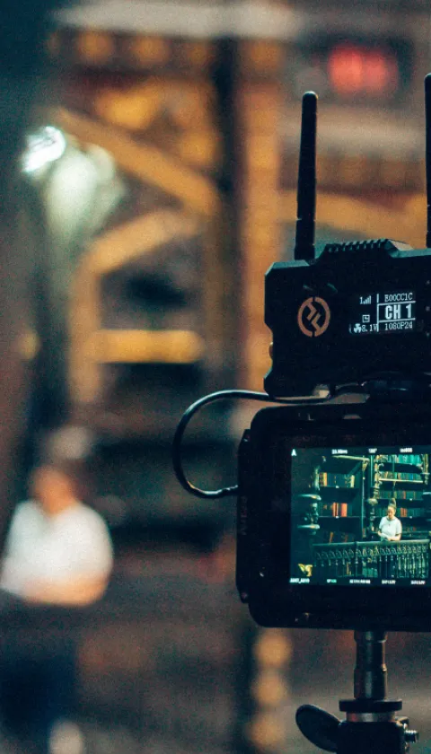 Close-up of a professional video camera recording a person in a blurred industrial interior, optimized for a vertical mobile layout.