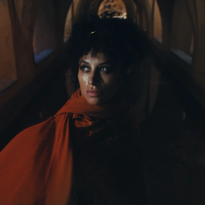 Woman wrapped in a red shawl standing beneath historic Andalusian arches, lit dramatically with a contemplative expression.