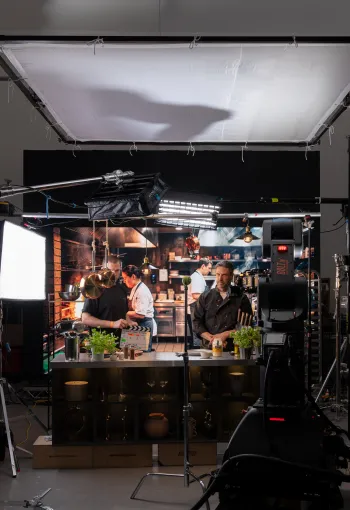 Behind-the-scenes view of a film studio set featuring a kitchen commercial shoot with chefs, studio lighting, and a high-speed motion control camera rig.