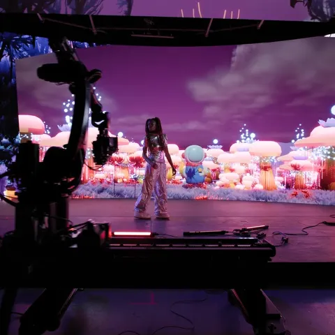 Camera rig filming a performer on a virtual production stage with illuminated LED screens and fantasy scenery.
